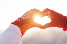 Person outdoors in snow, wearing gloves making heart shape with hands